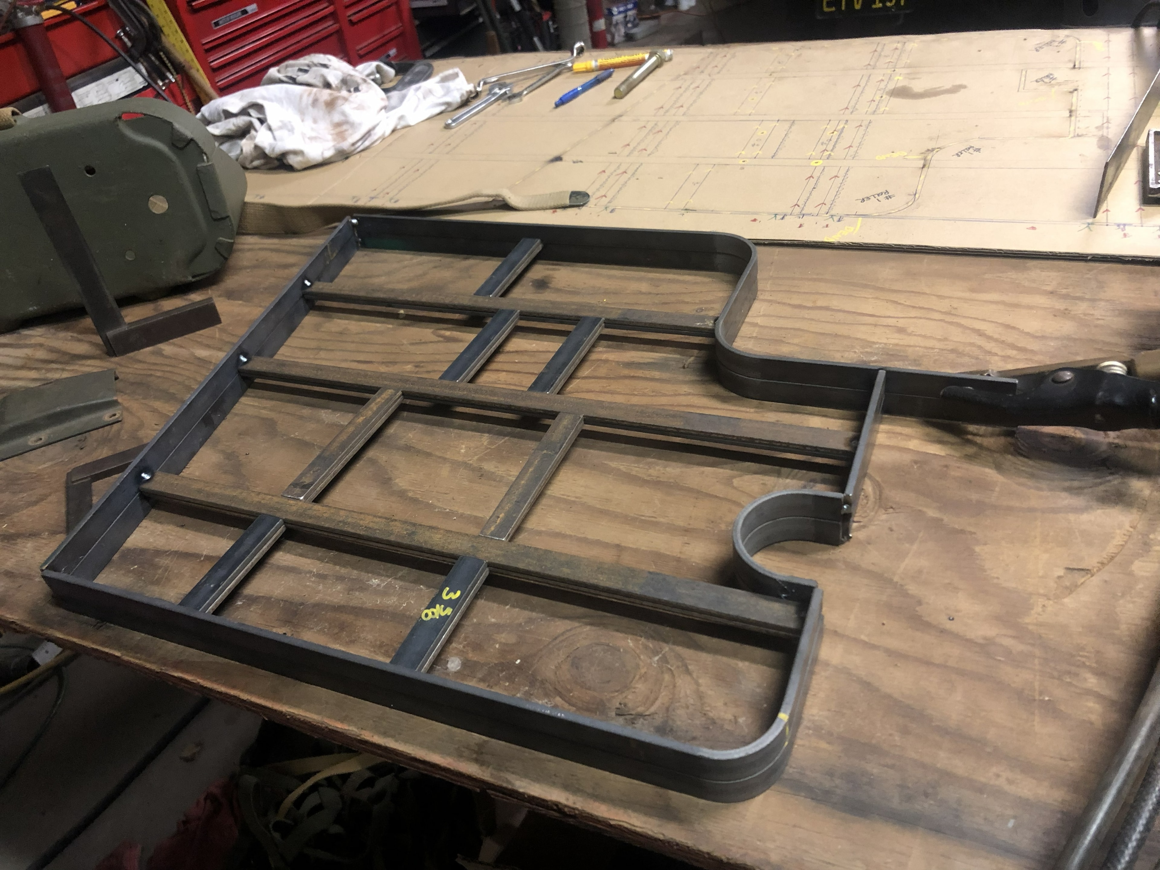 Fabricated bustle rack flat on workbench with engineering drawings
